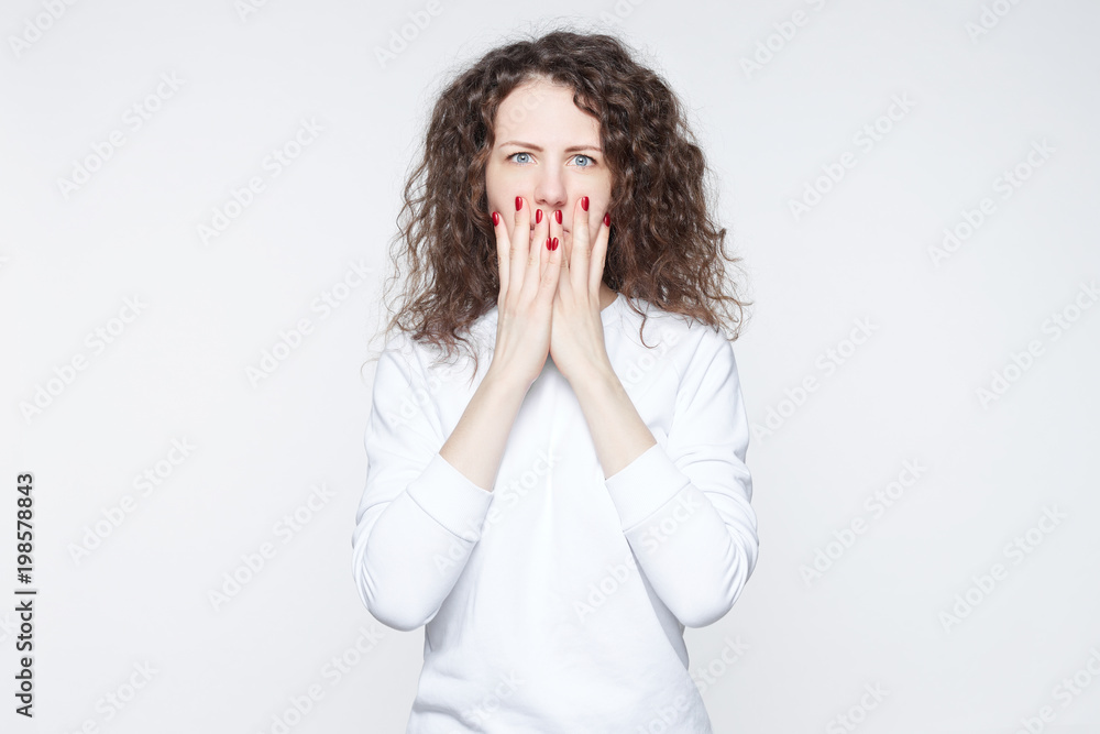 Close up portrait of upset scared European woman, covering mouth with both palms to prevent screaming sound, after seeing or hearing something bad. Negative emotions, facial expressions and feelings. Close up portrait of upset scared European woman, covering mouth with both palms to prevent screaming sound, after seeing or hearing something bad. Negative emotions, facial expressions and feelings.
