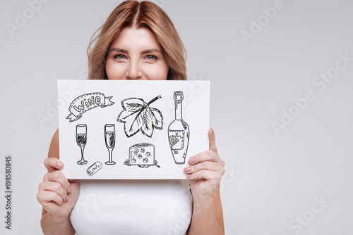Drinking wine. Adorable young smiling woman looking pleased while standing alone and thinking about drinking delicious wine