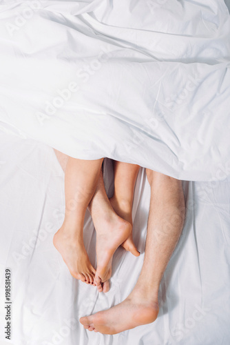 cropped shot of female and male legs in bed