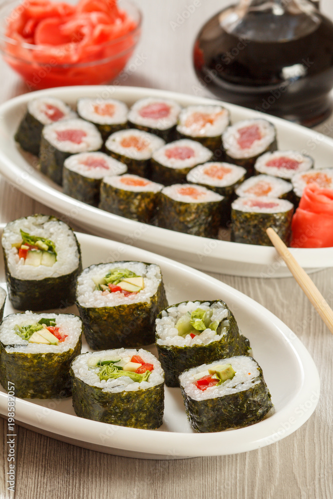 Different sushi rolls on ceramic plate, chopsticks, glass bottle with soy sauce and pickled ginger in a bowl Different sushi rolls on ceramic plate, chopsticks, glass bottle with soy sauce and pickled ginger in a bowl