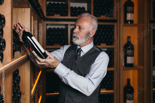 Mature sommelier choosing a bottle of wine at the wine cellar.  photo