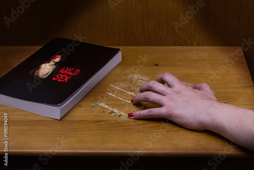 Woman's hand scratching a bedside table, where there is a book about wild sex.
