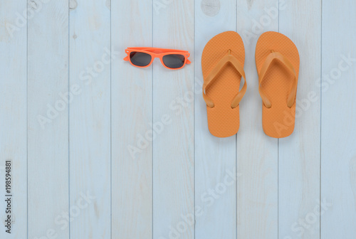 Artículos de ocio sobre fondo de madera azul: chanclas y gafas de sol de color naranja