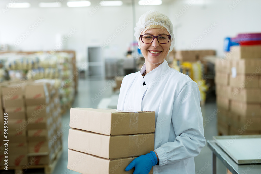 Young happy hard working female worker carrying a stack of boxes in factory storage room. Young happy hard working female worker carrying a stack of boxes in factory storage room.