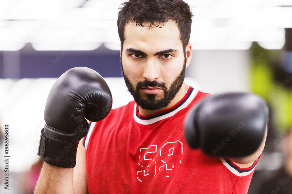 Bearded boxing man wears red shirt and black gloves in the ring