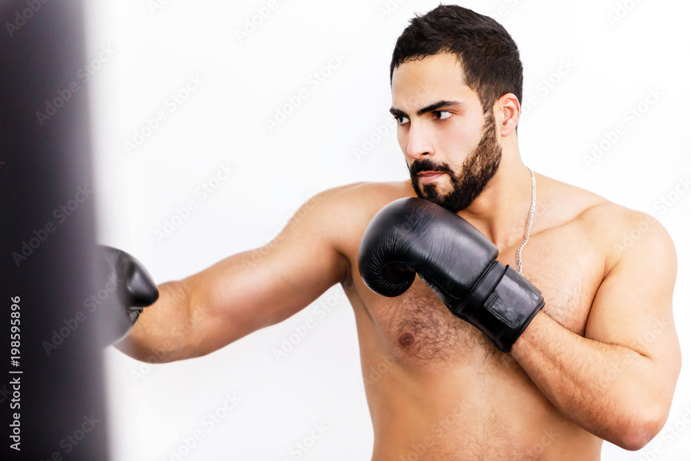 Muscular handsome topless boxer wears black gloves fights before white background