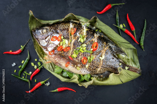 Traditional Thai barbecue tilapia fish staffed with coriander and chili as top view on a banana leaf