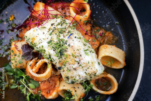 Braised codfish filet and lettuce and herbs with calamarata noodles as top view on a plate photo