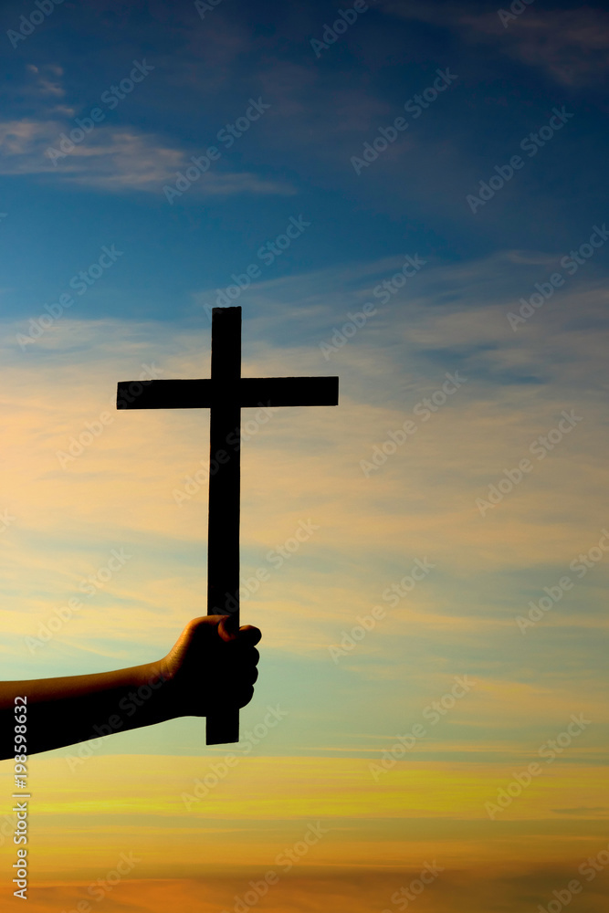 Silhouette of hand holding cross on sunset background