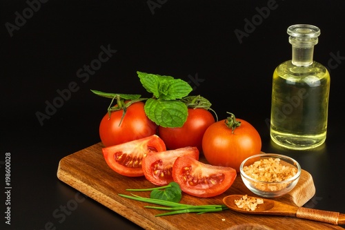 Tomatoes and herbs on a kitchen board. Preparation of healthy food. Raw vegetables. On a black background.