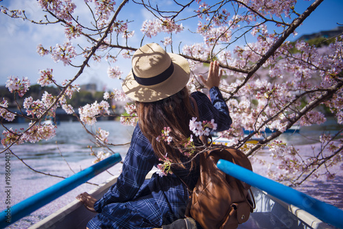 Hipster woman is sightseeing cherry blossom on the row boat while traveling during spring season at Chidorigafuchi boat parking inside the Kitanomaru Park in Tokyo, Japan.