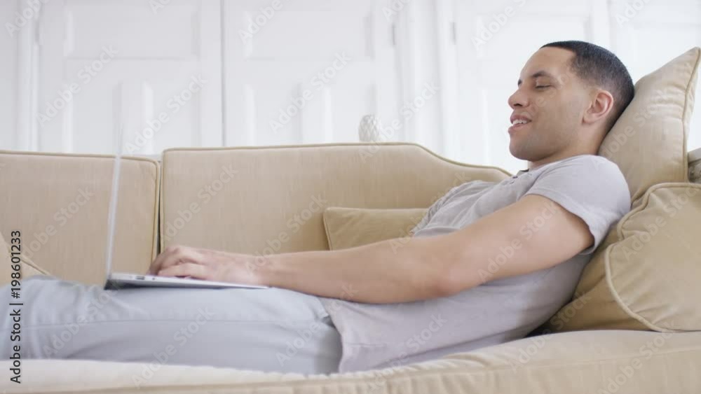 Handsome young male relaxing on the couch on his laptop Handsome young male relaxing on the couch on his laptop