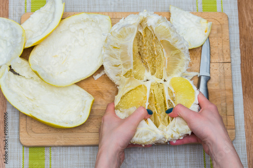 Girl cleans a pomelo on a wooden board photo