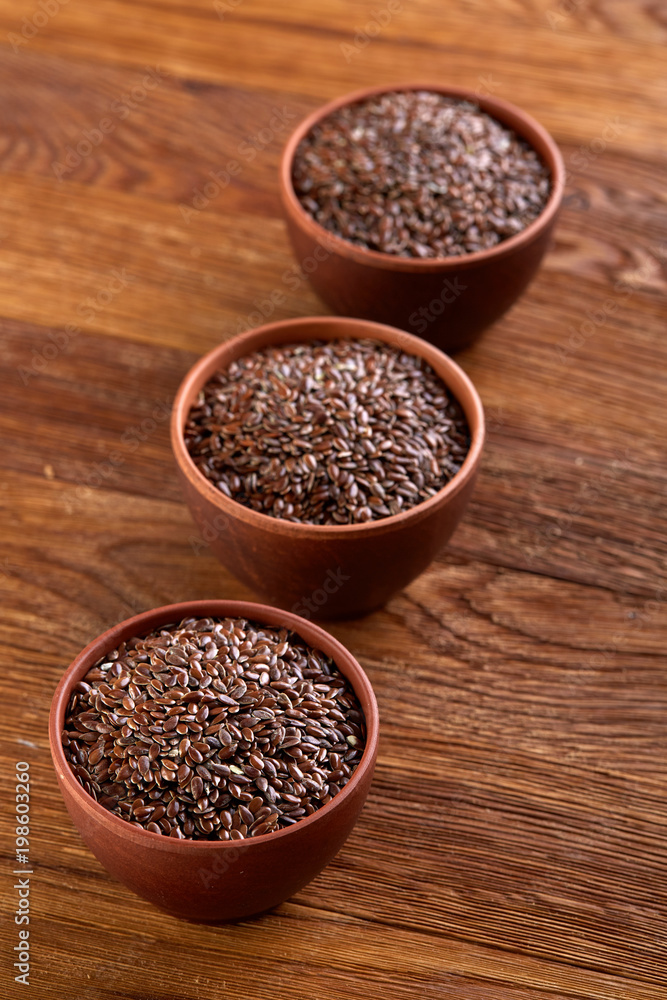 Three ceramic bowls with flaxseeds arrenged in row over wooden background, top view, selective focus Three ceramic bowls with flaxseeds arrenged in row over wooden background, top view, selective focus