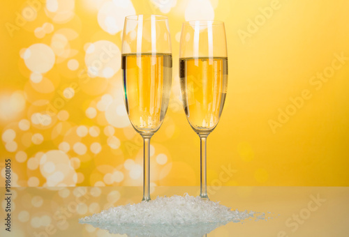Two wonderful wineglass of champagne with bubbles of air, near handful of artificial snow on bright yellow