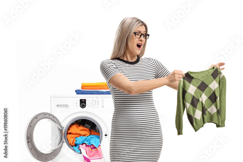 Фотография Shocked young woman holding a shrunken blouse in front of washing machine