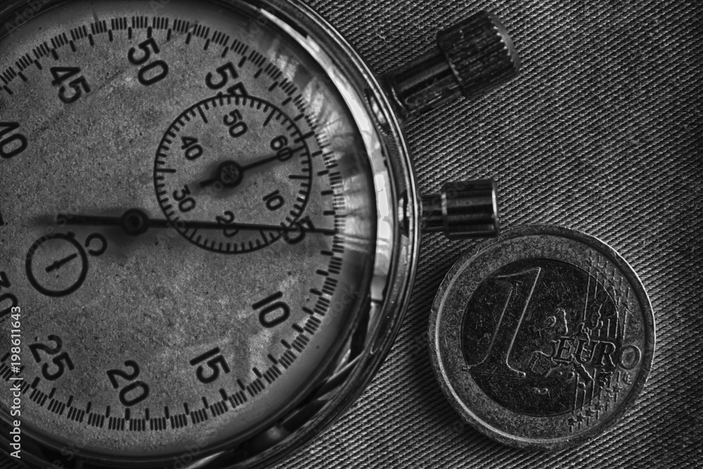 Euro coin with a denomination of 1 euro and stopwatch on denim backdrop - business background Euro coin with a denomination of 1 euro and stopwatch on denim backdrop - business background