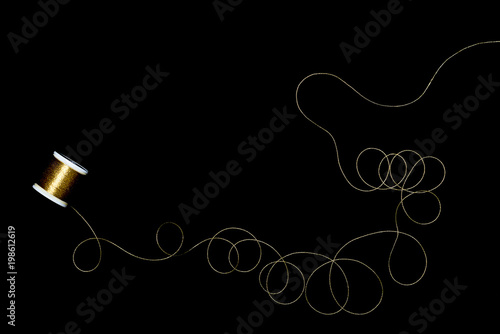 Spool of gold thread on a black background.	