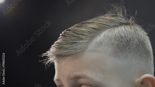 Hairdresser makes hairstyle for boy with a hair dryer and a comb. Cute kid in barbershop. New hairstyle photo