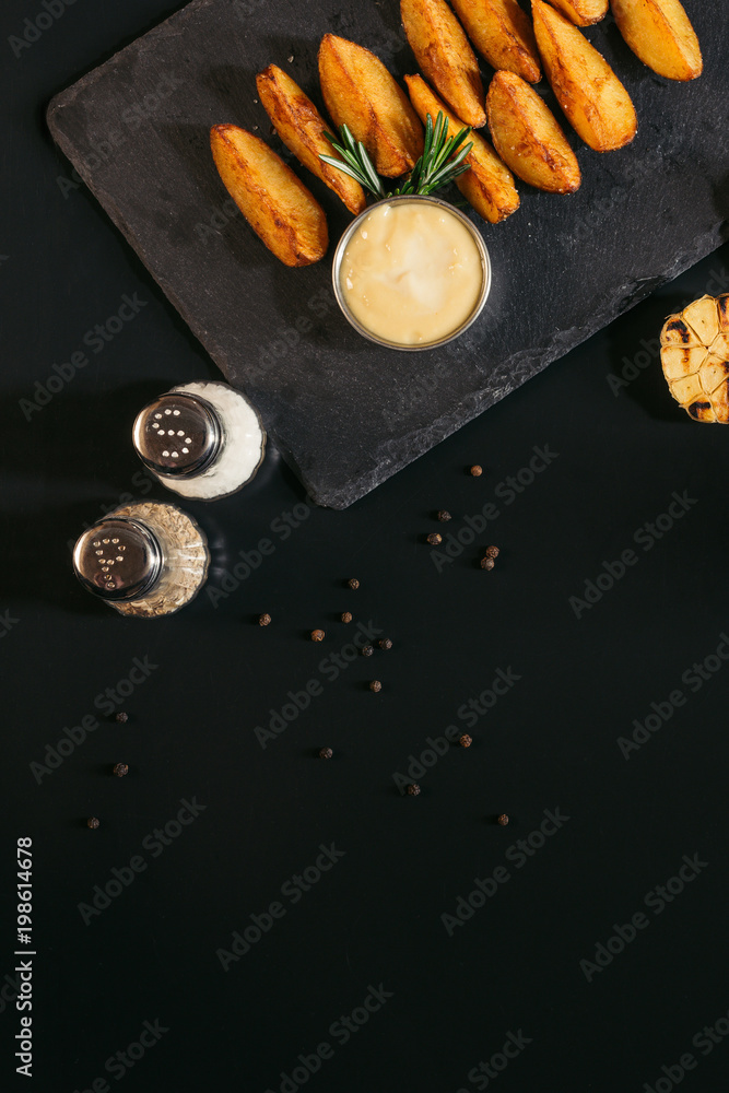 top view of spices, baked potatoes with sauce and grilled garlic on black top view of spices, baked potatoes with sauce and grilled garlic on black