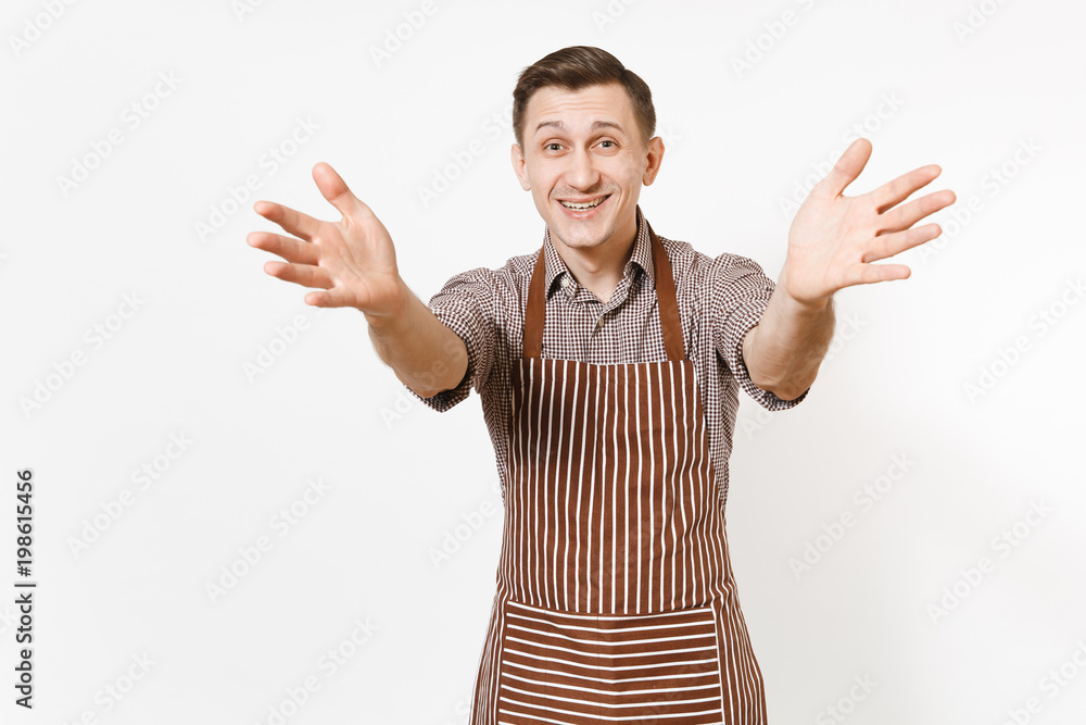 Young happy smiling man chef or waiter in striped brown apron, shirt stretching hands to camera isolated on white background. Male good housekeeper or houseworker. Domestic worker for advertisement. Young happy smiling man chef or waiter in striped brown apron, shirt stretching hands to camera isolated on white background. Male good housekeeper or houseworker. Domestic worker for advertisement.