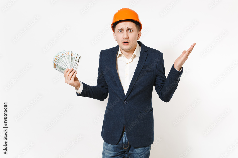 Young handsome shocked businessman in dark suit, protective construction helmet holding bundle of dollars, cash money isolated on white background. Male worker for advertisement. Business concept. Young handsome shocked businessman in dark suit, protective construction helmet holding bundle of dollars, cash money isolated on white background. Male worker for advertisement. Business concept.