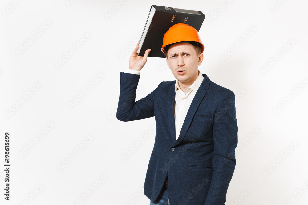 Concerned dissatisfied businessman in dark suit, protective hardhat holding black folder for papers document near head isolated on white background. Male worker for advertisement. Business concept. Concerned dissatisfied businessman in dark suit, protective hardhat holding black folder for papers document near head isolated on white background. Male worker for advertisement. Business concept.