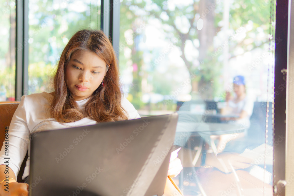 beautiful asian young business woman sitting near transparent window and using laptop for her job at cafe or coffee shop. business concept. beautiful asian young business woman sitting near transparent window and using laptop for her job at cafe or coffee shop. business concept.