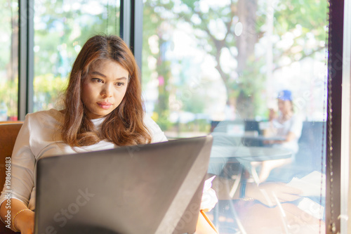 beautiful asian young business woman sitting near transparent window and using laptop for her job at cafe or coffee shop. business concept.