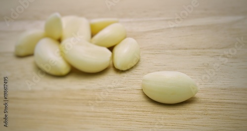 A peeled garlic clove on wooden table, with blurred garlic heap as background. Herbal plants and healthy food related to blood pressure, antibiotics, etc.