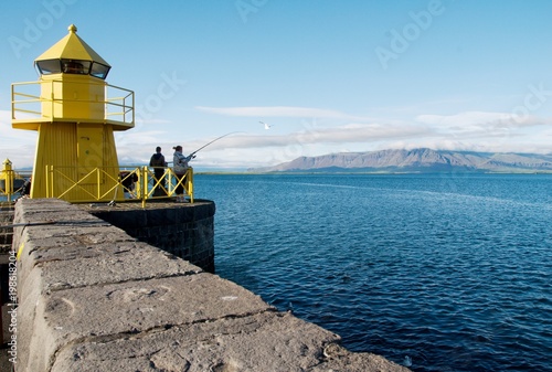 Angler am gelben Leuchturm im Hafen Reykjavik, Island