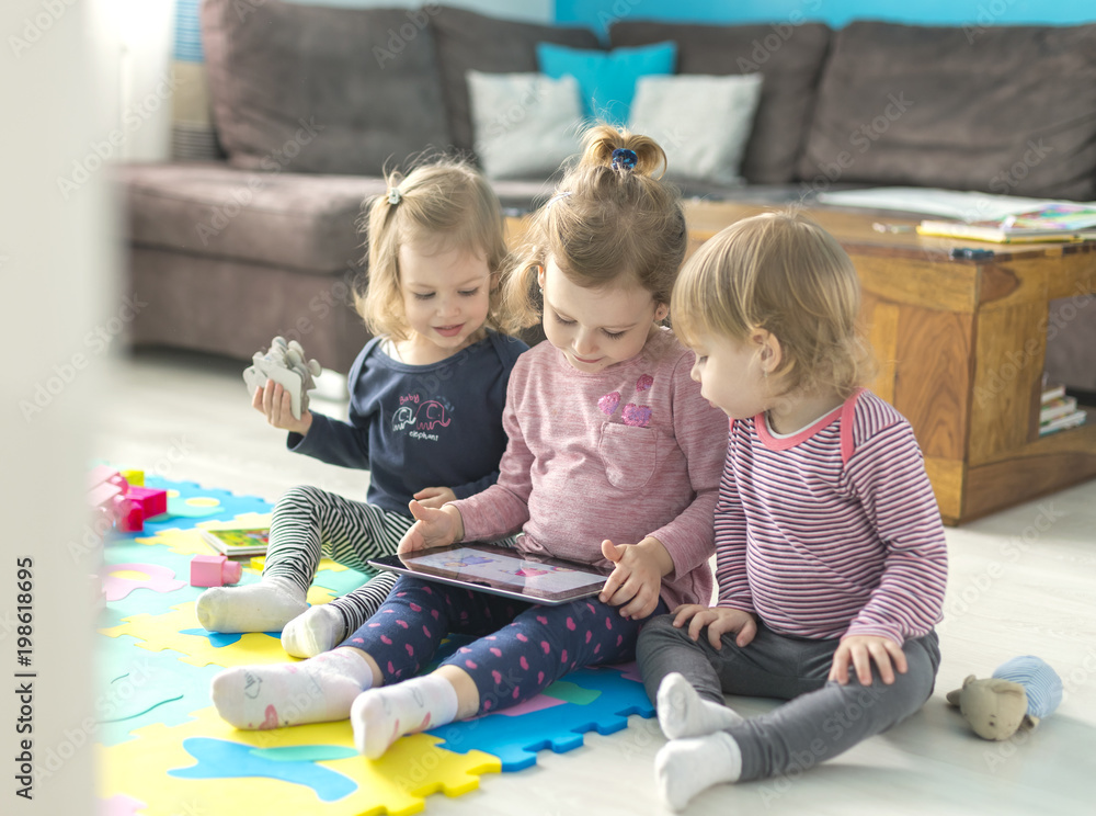 Naklejka premium Three little sisters use tablet at home