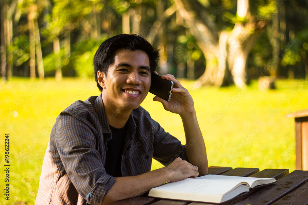 Closeup shot of smiling young Malay man using smartphone while sitting Closeup shot of smiling young Malay man using smartphone while sitting