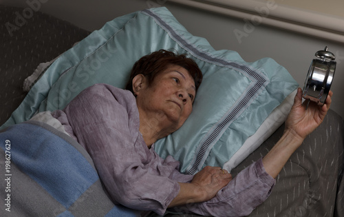 Restless senior woman glaring at alarm clock during nighttime while in bed