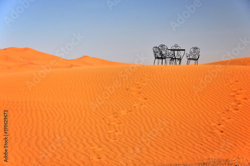 Metal chairs and tables are abandoned on the sand dune in the Sahara. Erg Chebbi, Morocco, Africa.