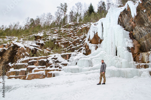 Young man tourist walking on nature of reserve Stolby. On mountaain and ice waterfall background. photo