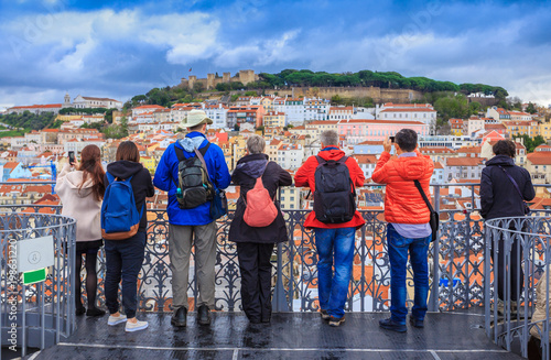 Group of tourists watching the cityscape of Lisbon and taking pictures to Sao Jorge castle in Portugal