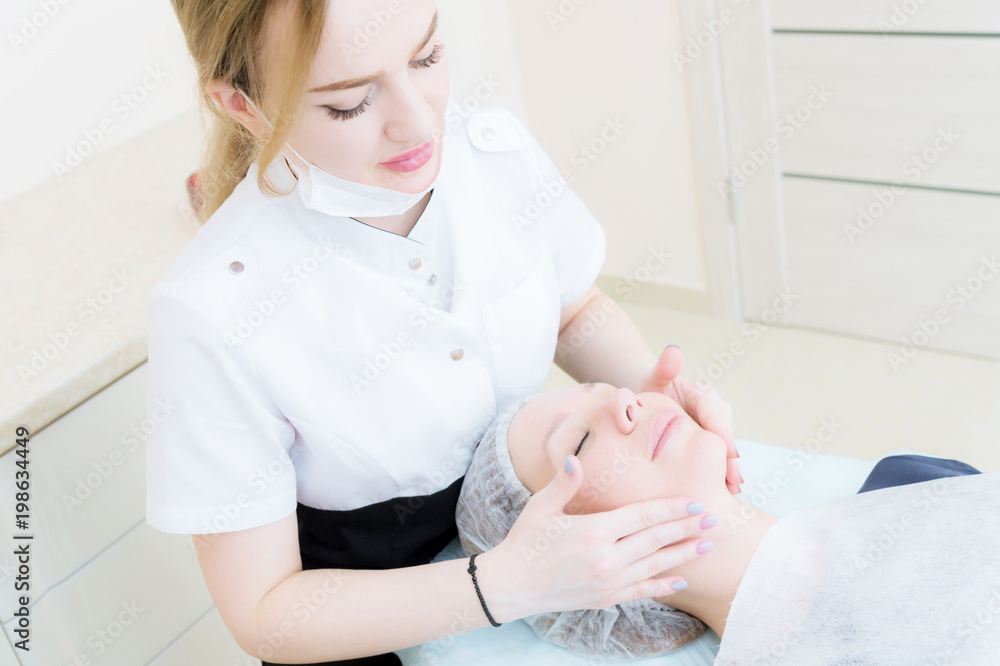 Beauty saloon. Close-up of a medical beautician in pink gloves makes a face massage of a beautiful woman. Cosmetology. Head and shoulders of a girl with closed eyes. The concept of women's beauty and Beauty saloon. Close-up of a medical beautician in pink gloves makes a face massage of a beautiful woman. Cosmetology. Head and shoulders of a girl with closed eyes. The concept of women's beauty and