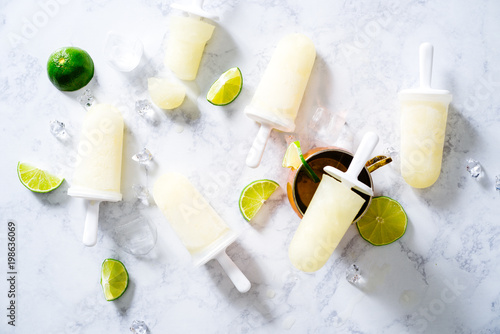 Photography Summertime moscow mule popsicles with lime wedges on white marble surface with copper mug