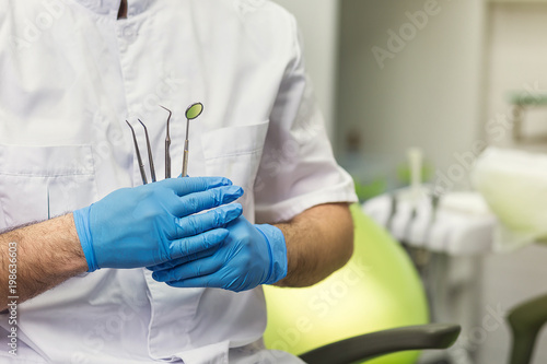 Male dentist with tools over medical office background. Healthcare, profession, stomatology and medicine concept