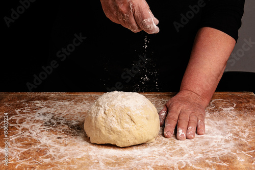 The hands of an old grandmother sprinkle with flour dough