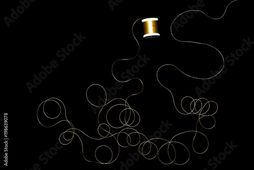 Spool of gold thread on a black background.	