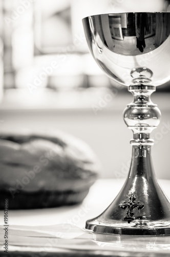 Up close shot of gleaming communion chalice with loaf of communion bread in the background.