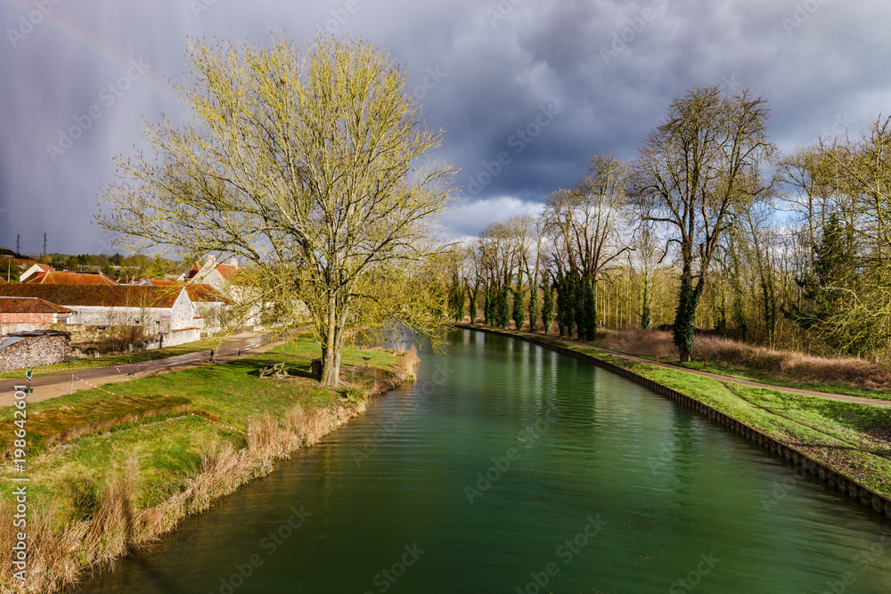 Green water of canal and blue sky, springtime in countryside