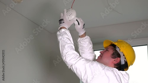 Young male electrician installing fire smoke sensor