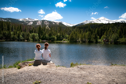 little girls sitting by a mountain lake