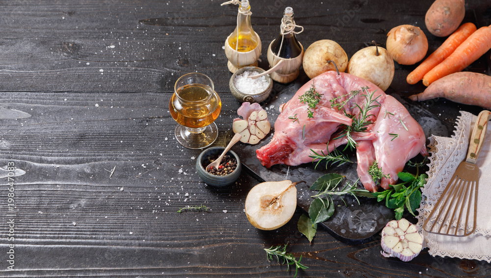 Whole Forest wild rabbit, Recipe with apple pie, Raw meat with spices and vegetables, Sea salt, red, white pepper and coriander in clay pots on an old black rustic table. copy space Whole Forest wild rabbit, Recipe with apple pie, Raw meat with spices and vegetables, Sea salt, red, white pepper and coriander in clay pots on an old black rustic table. copy space