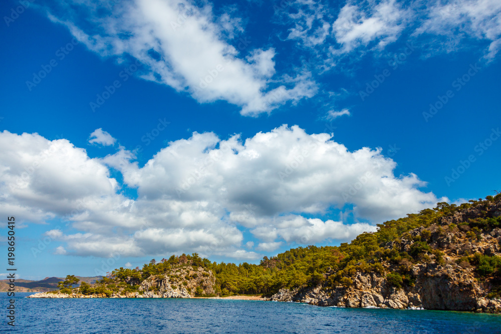 Naklejka premium Rocky coast with trees in the Aegean Sea. Big beautiful white clouds