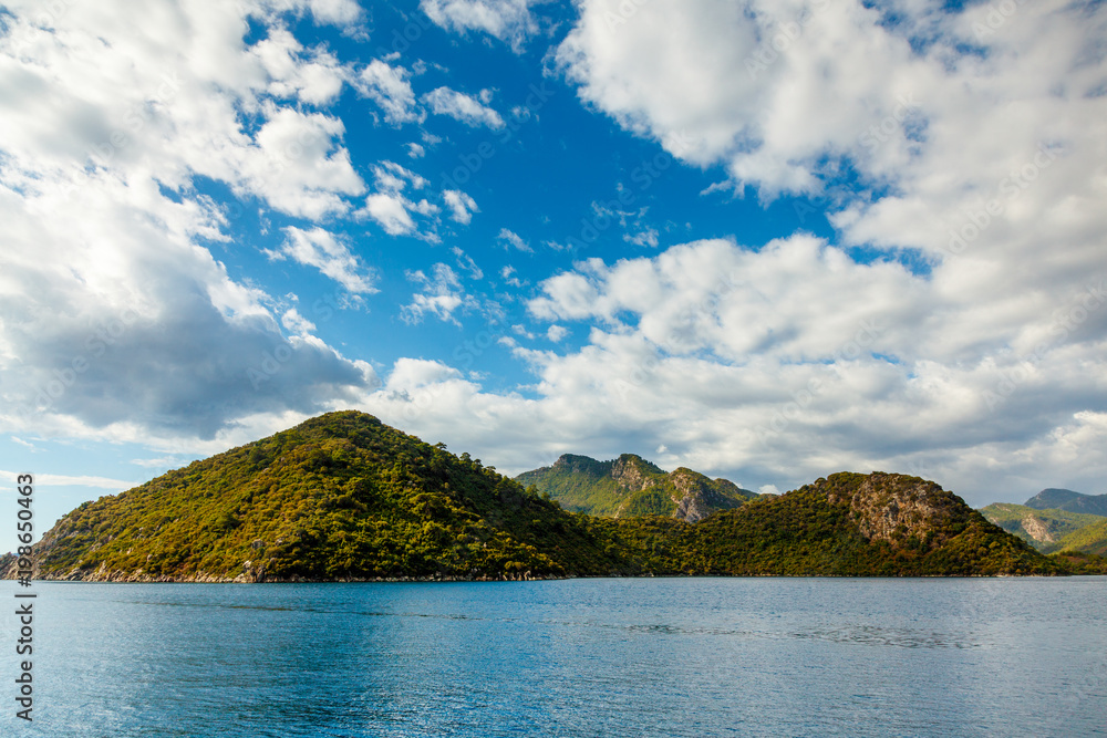 Rocky coast with trees in the Aegean Sea. Big beautiful white clouds