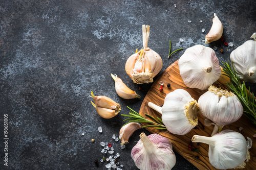 Garlic cloves with spices and herbs on a dark stone background. 